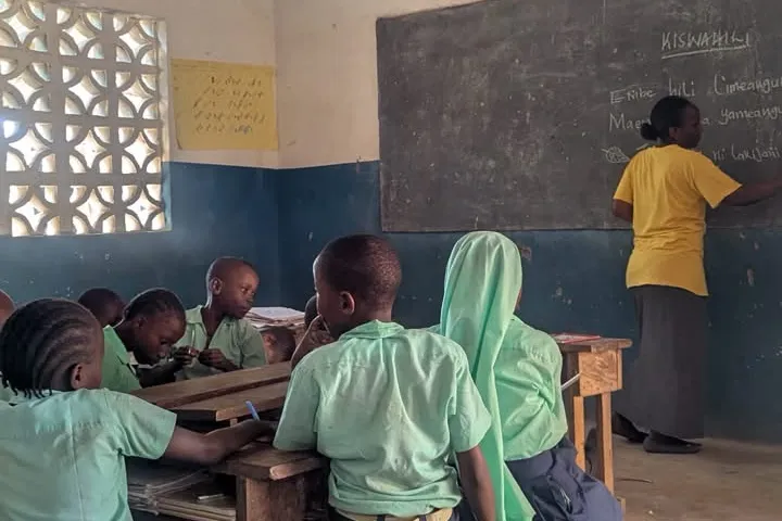 Una clase de suajili en un aula de Daystar Nursery School: alumnos con uniforme en sus pupitres mientras la maestra escribe en el pizarrón