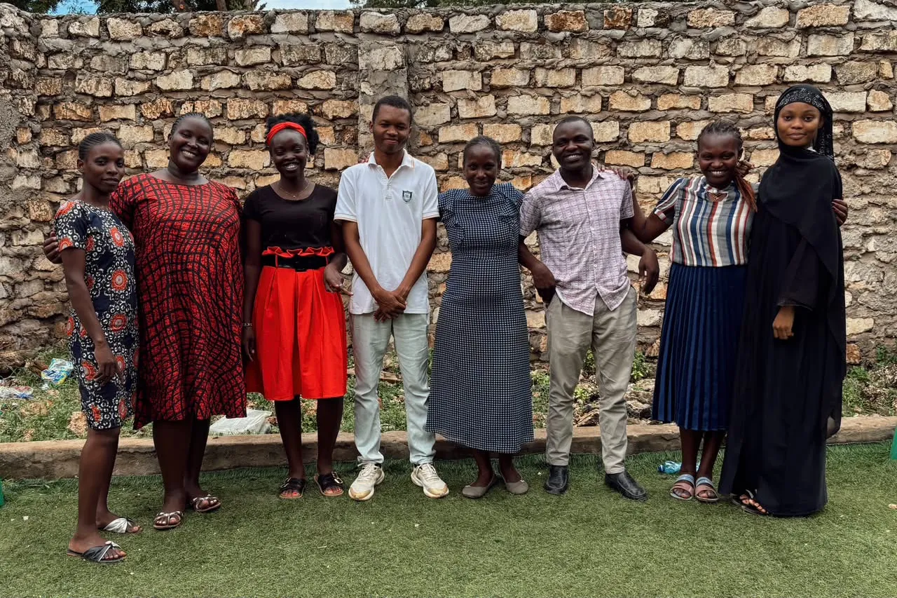 El equipo docente de Daystar, de pie frente al muro de piedra de la escuela